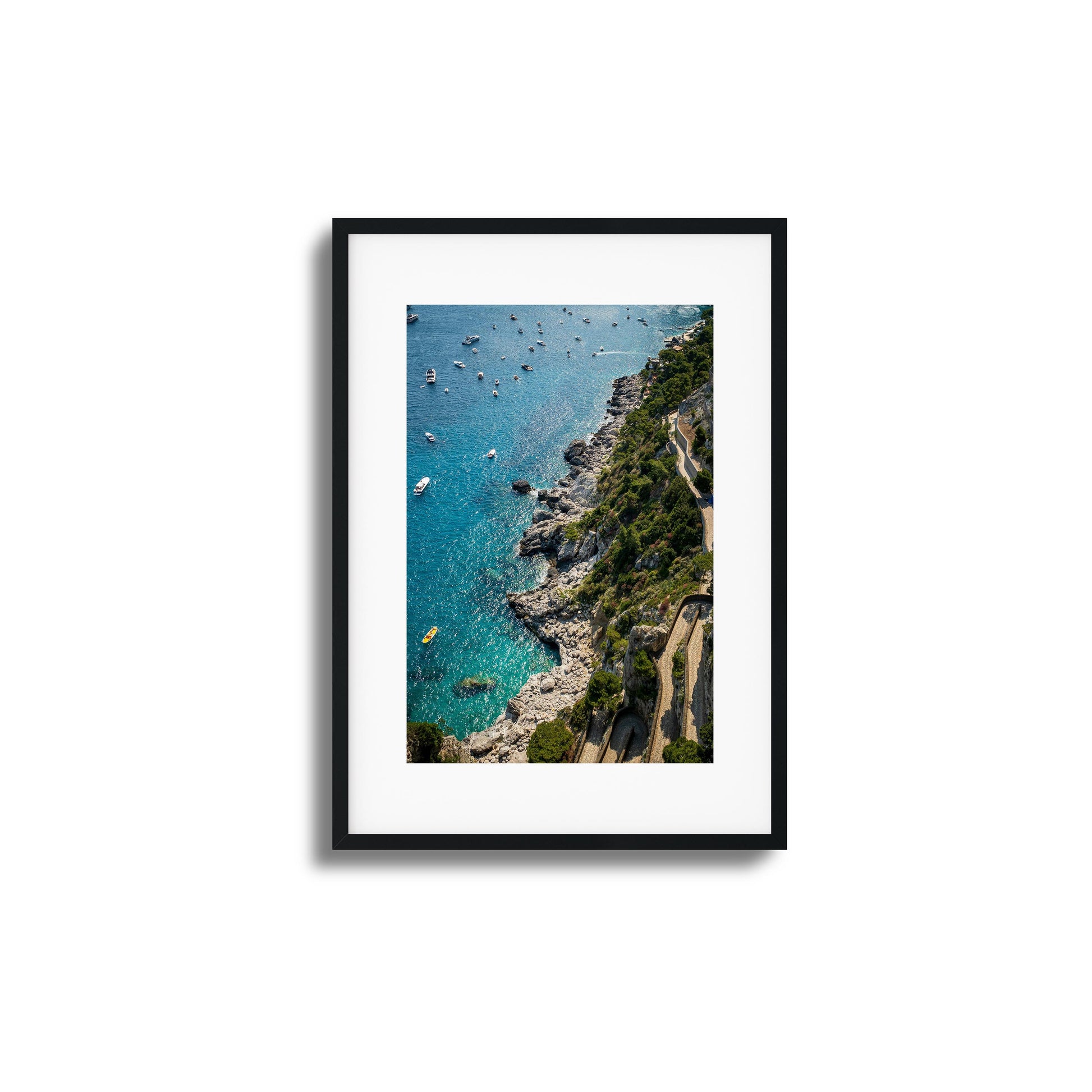 A stunning aerial view of turquoise Mediterranean waters, rocky cliffs, and scattered boats, framed artwork.