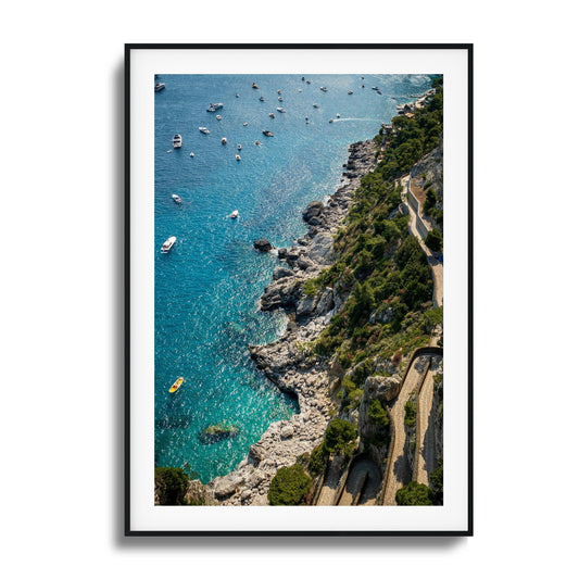 A stunning aerial view of turquoise Mediterranean waters, rocky cliffs, and scattered boats, framed artwork.