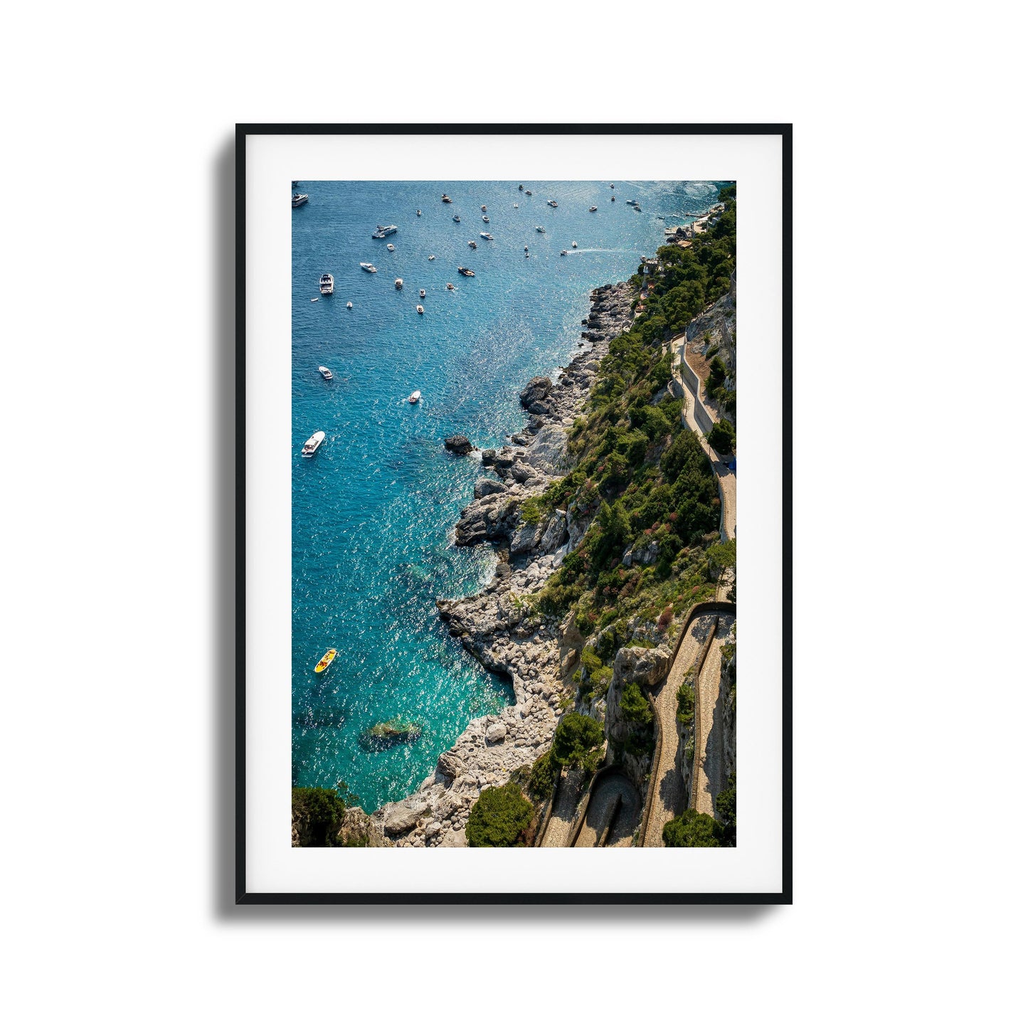 A stunning aerial view of turquoise Mediterranean waters, rocky cliffs, and scattered boats, framed artwork.