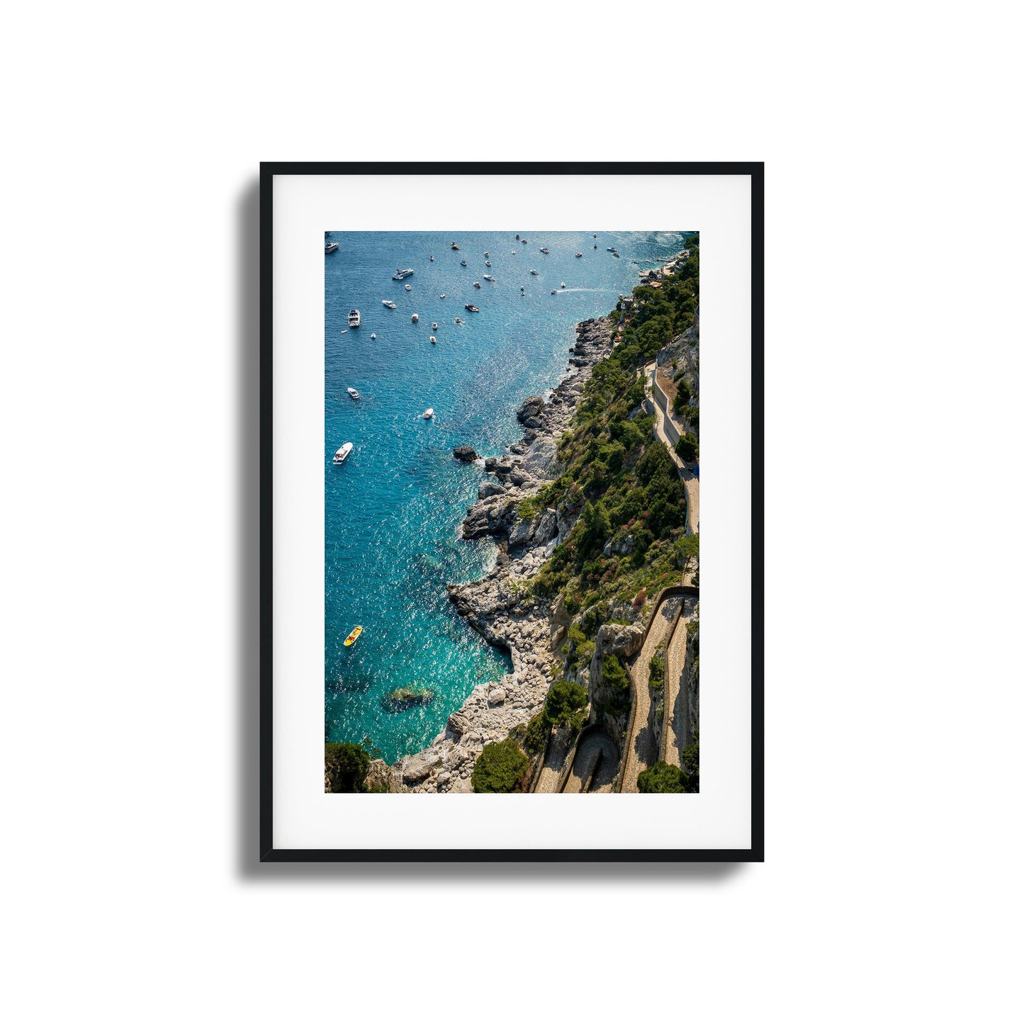 A stunning aerial view of turquoise Mediterranean waters, rocky cliffs, and scattered boats, framed artwork.