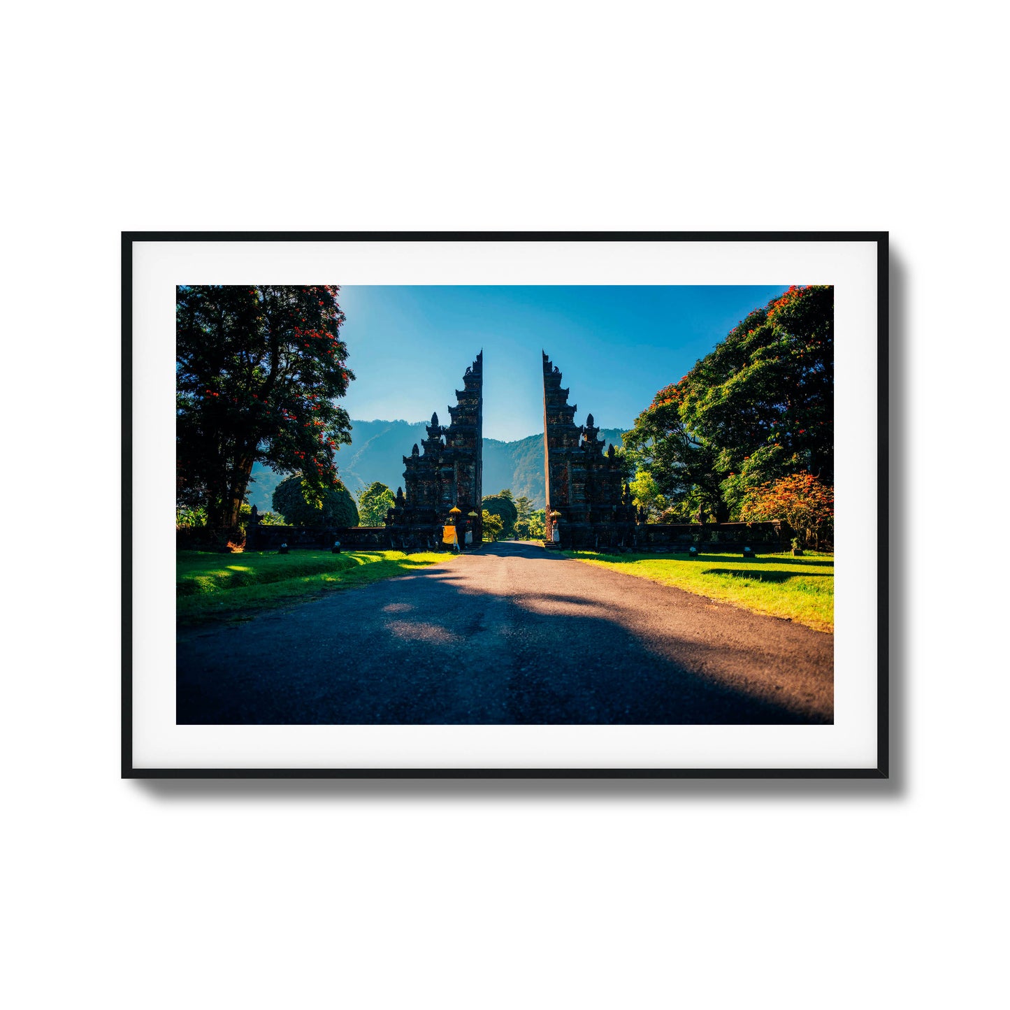 Balinese gates with a scenic mountain backdrop, surrounded by trees and sunshine, framed art.