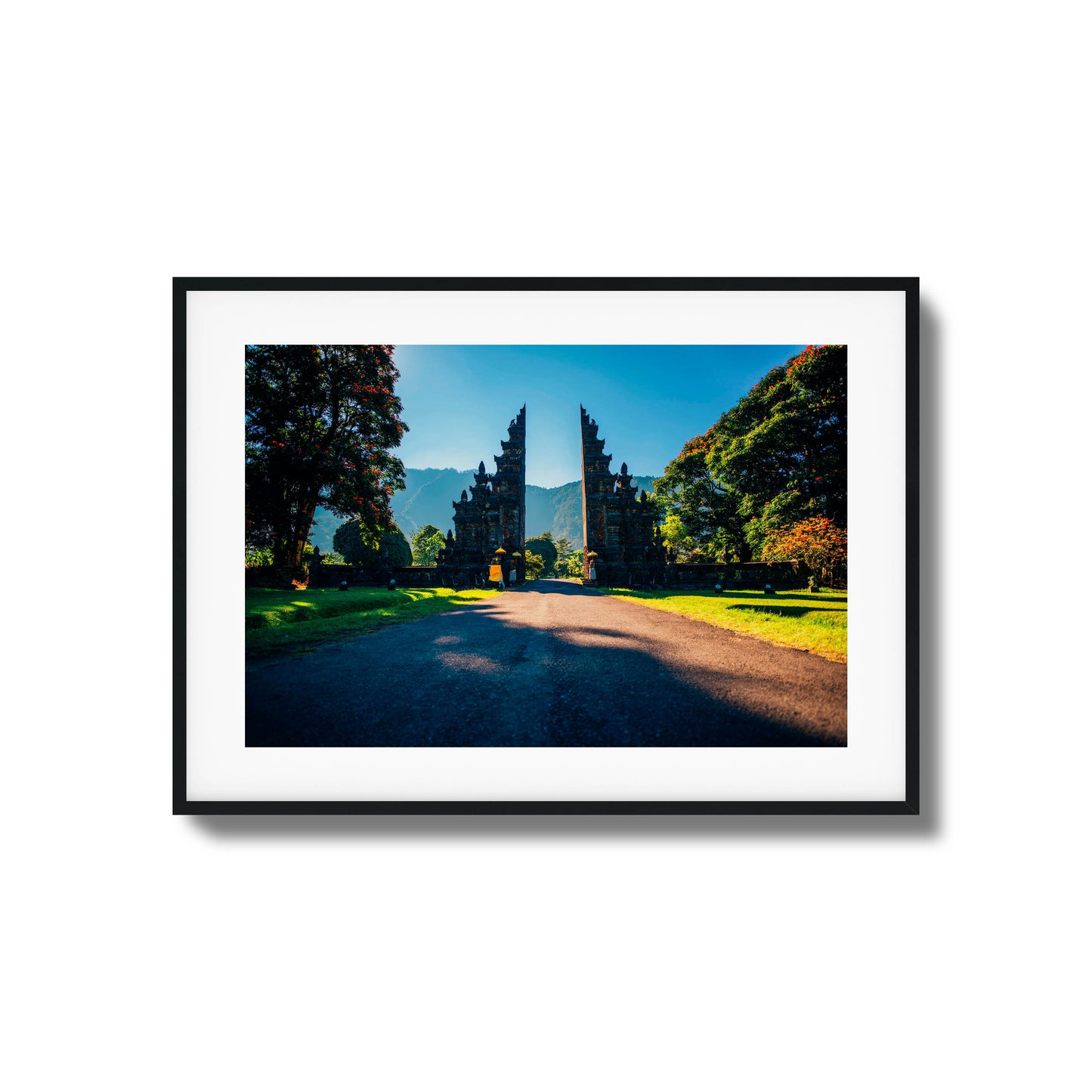 Balinese gates with a scenic mountain backdrop, surrounded by trees and sunshine, framed art.