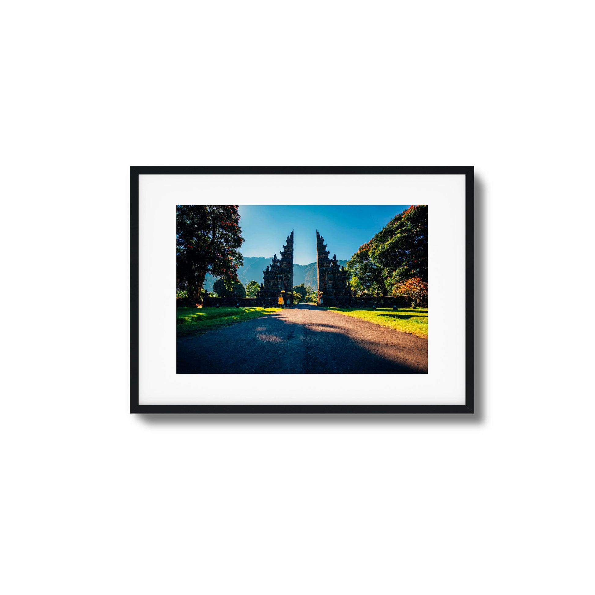 Balinese gates with a scenic mountain backdrop, surrounded by trees and sunshine, framed art.