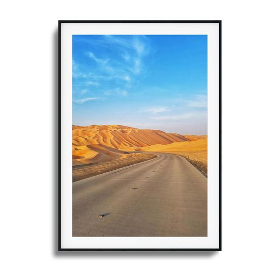 A paved road turning into tall sand dunes framed under a blue sky