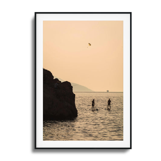 Paddleboarders and a parasail over calm waters during a golden sunset, perfect for framed wall art.