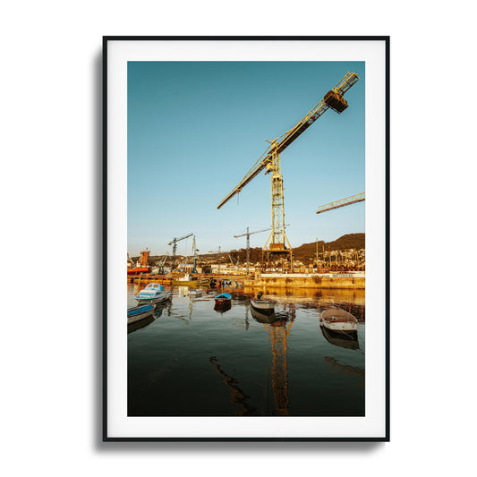 Boats and cranes lit by a rising sun over a harbor