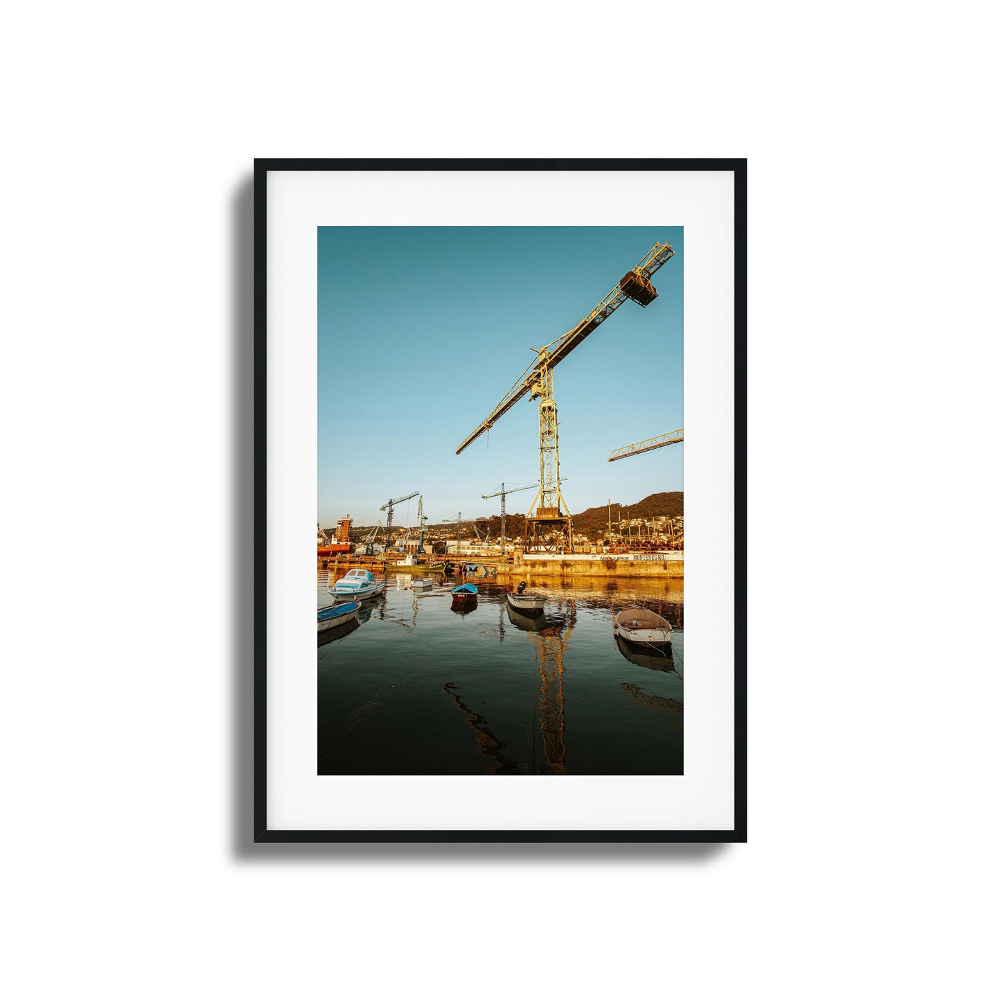 Boats and cranes lit by a rising sun over a harbor