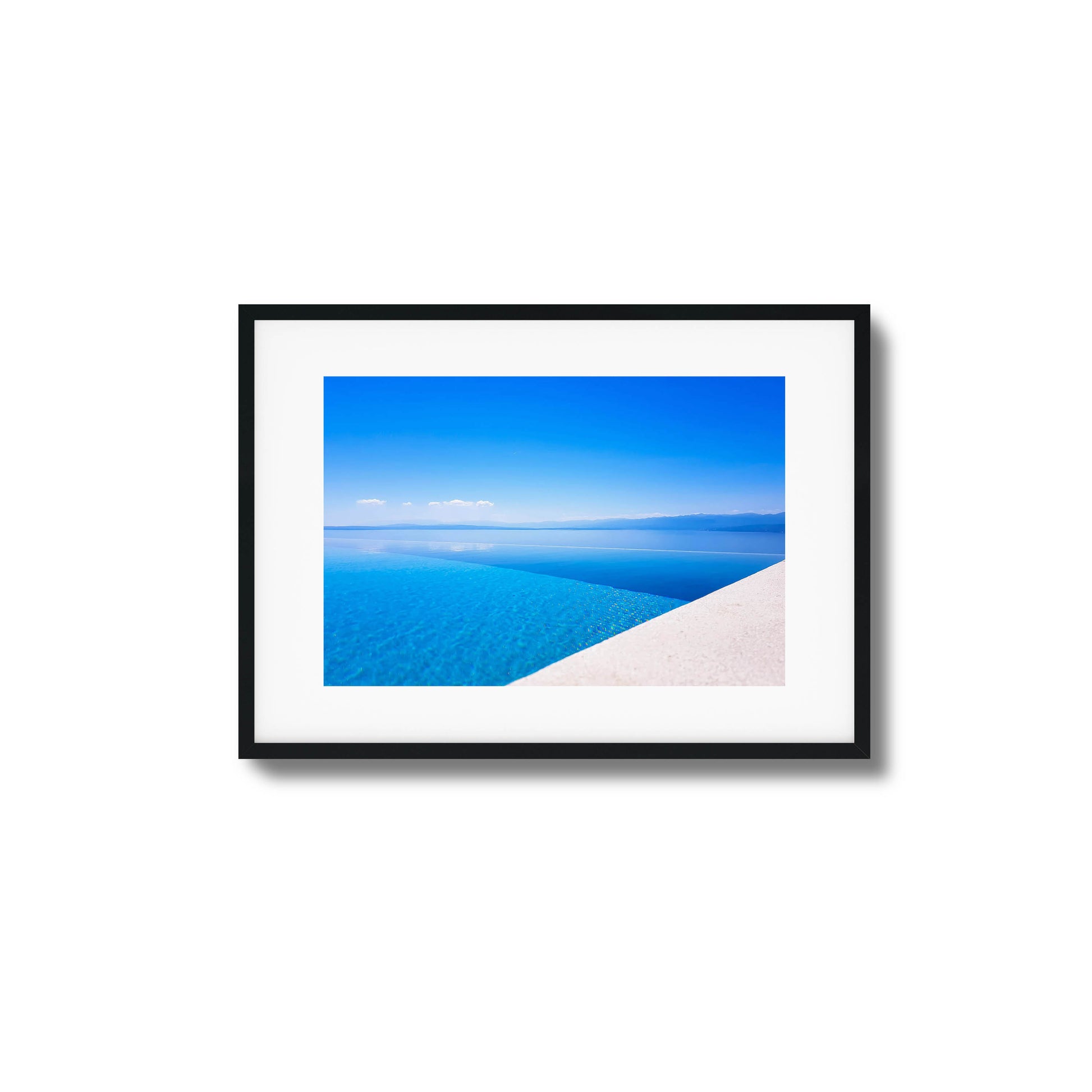 Infinity pool with crystal-clear blue water blending into the sea and distant mountains, framed art.