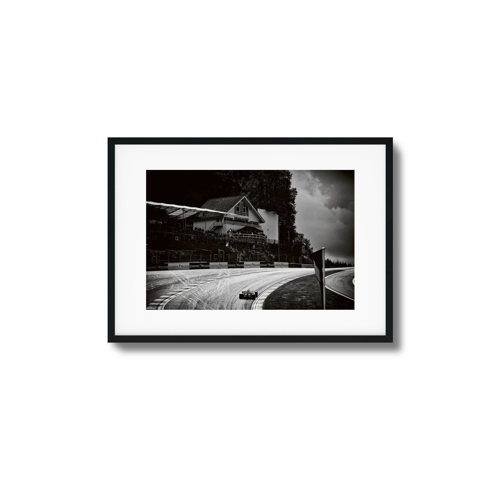 Black-and-white photo of a racecar speeding through a scenic racetrack, framed artwork.