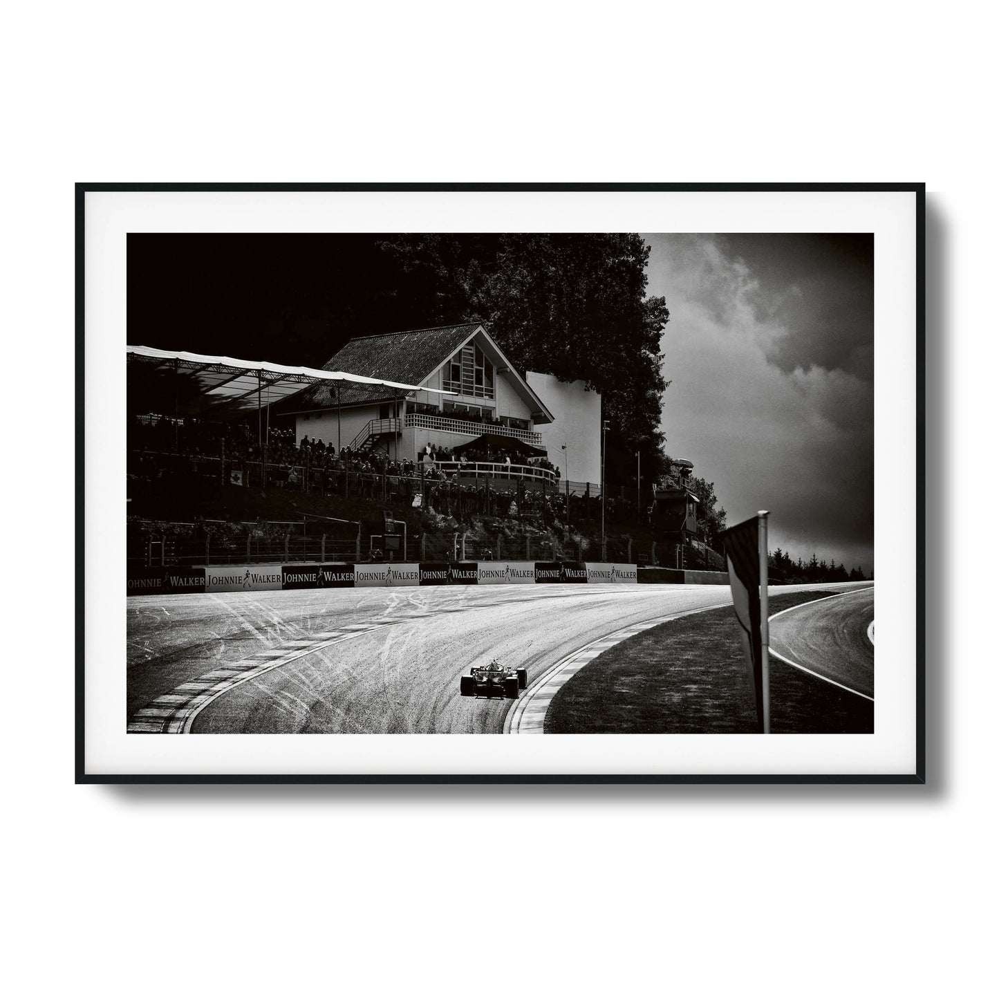 Black-and-white photo of a racecar speeding through a scenic racetrack, framed artwork.