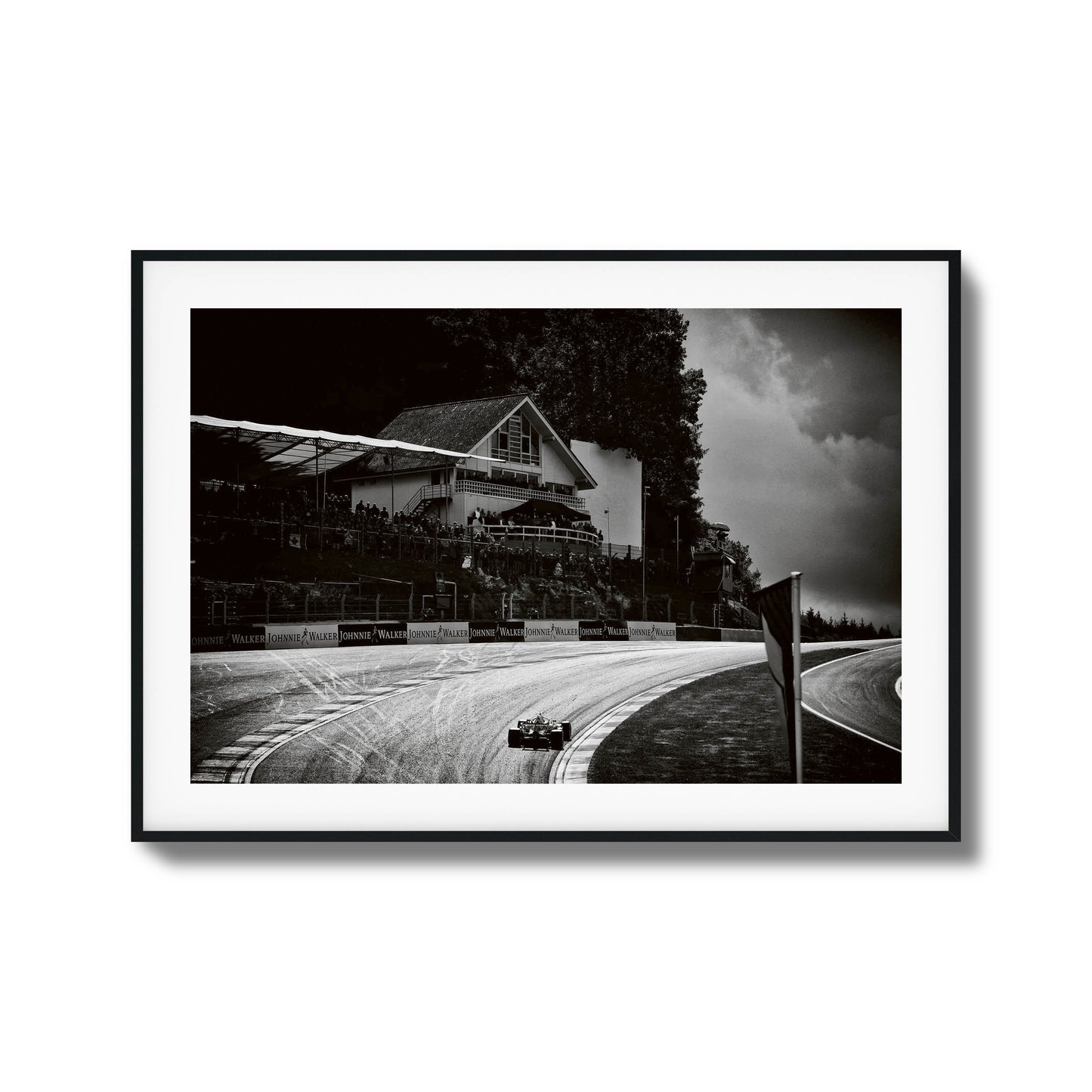 Black-and-white photo of a racecar speeding through a scenic racetrack, framed artwork.