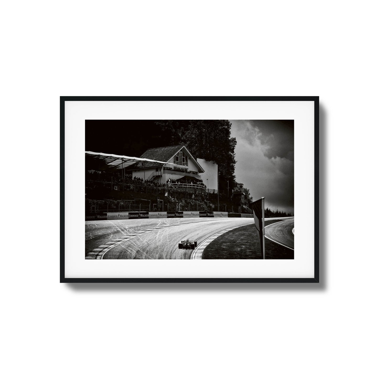 Black-and-white photo of a racecar speeding through a scenic racetrack, framed artwork.