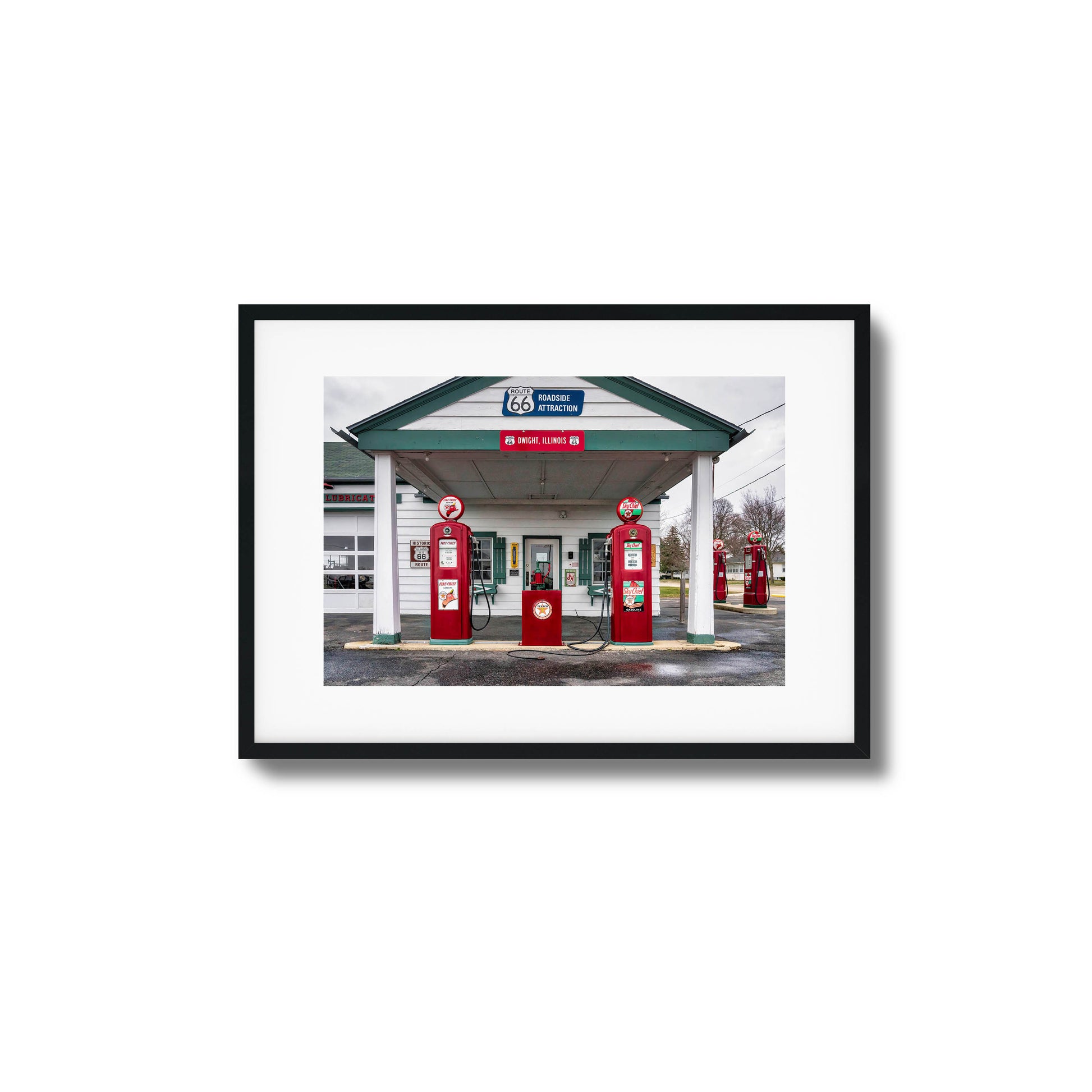 A vintage gas station on Route 66 with red fuel pumps and classic signage, framed artwork.