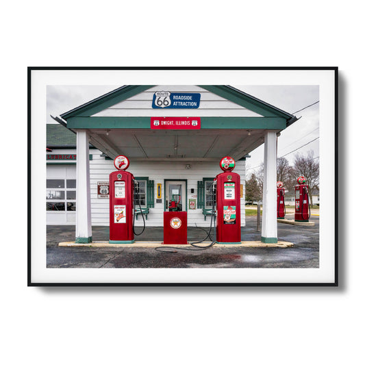 A vintage gas station on Route 66 with red fuel pumps and classic signage, framed artwork.