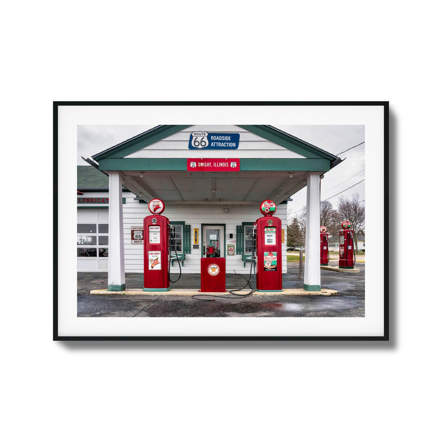 A vintage gas station on Route 66 with red fuel pumps and classic signage, framed artwork.