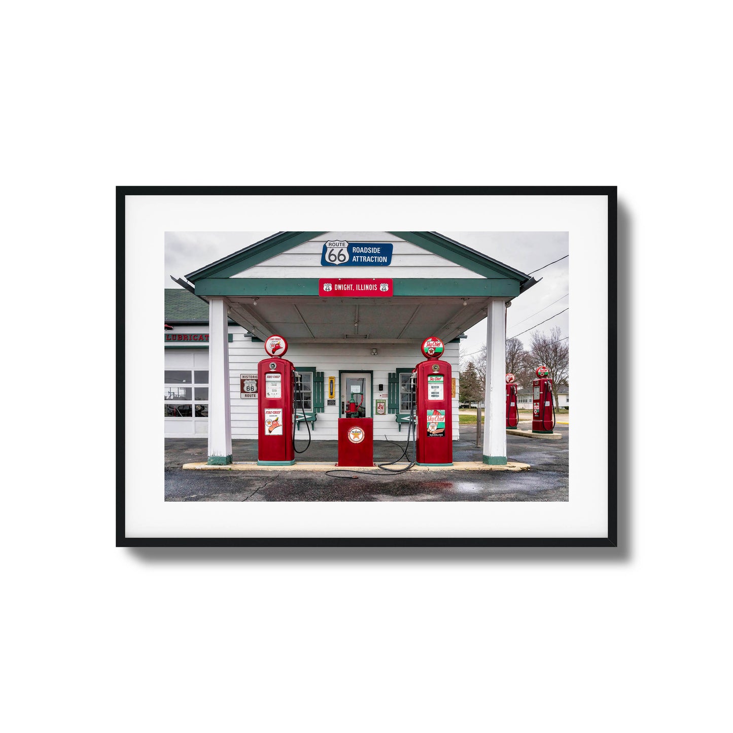 A vintage gas station on Route 66 with red fuel pumps and classic signage, framed artwork.