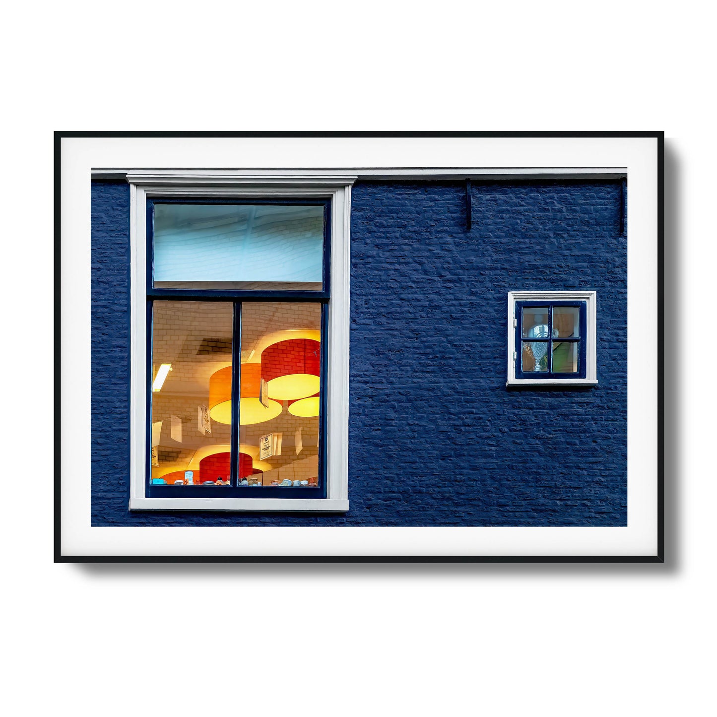 Close-up of a blue brick wall with glowing windows reflecting vibrant interiors, framed art.