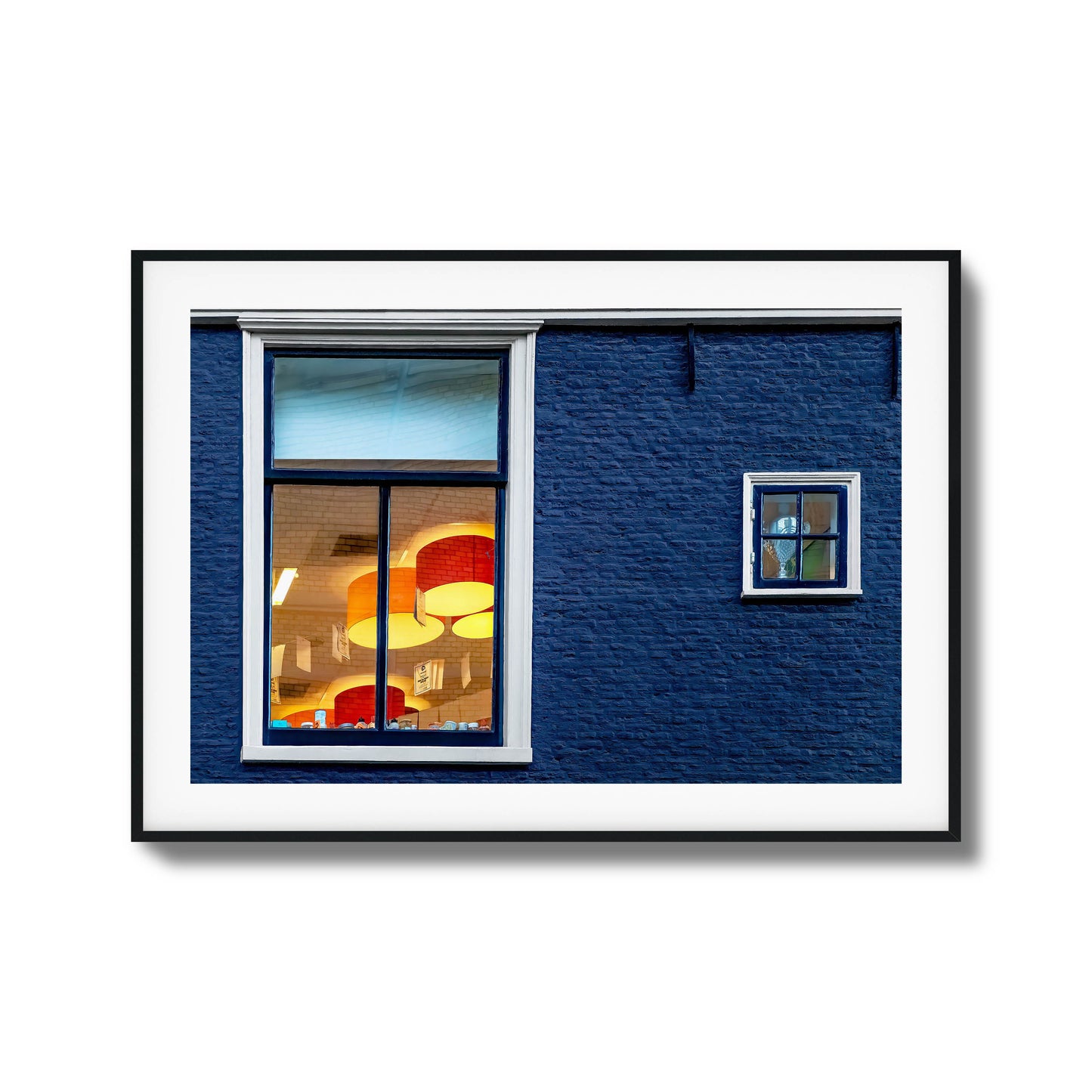 Close-up of a blue brick wall with glowing windows reflecting vibrant interiors, framed art.