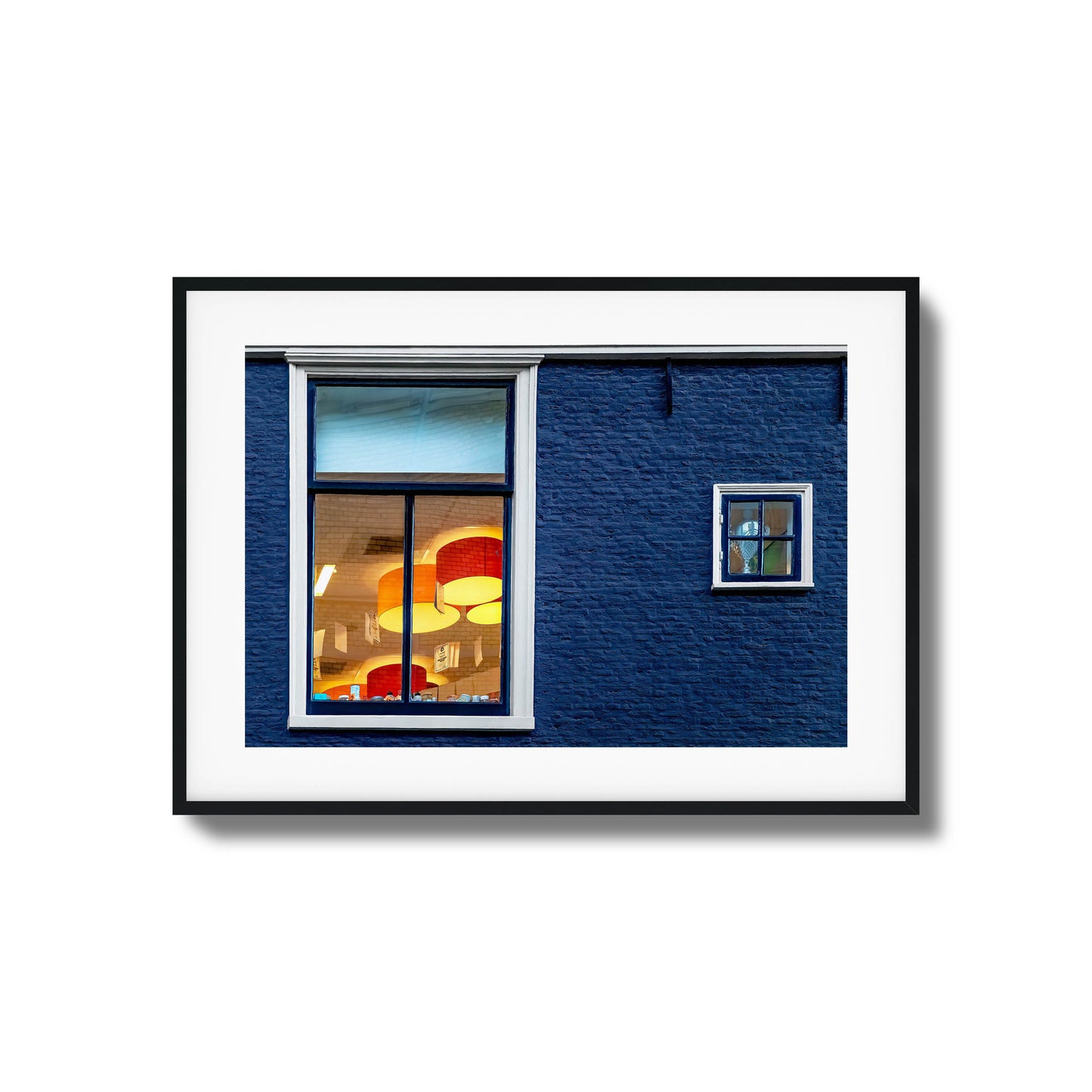 Close-up of a blue brick wall with glowing windows reflecting vibrant interiors, framed art.